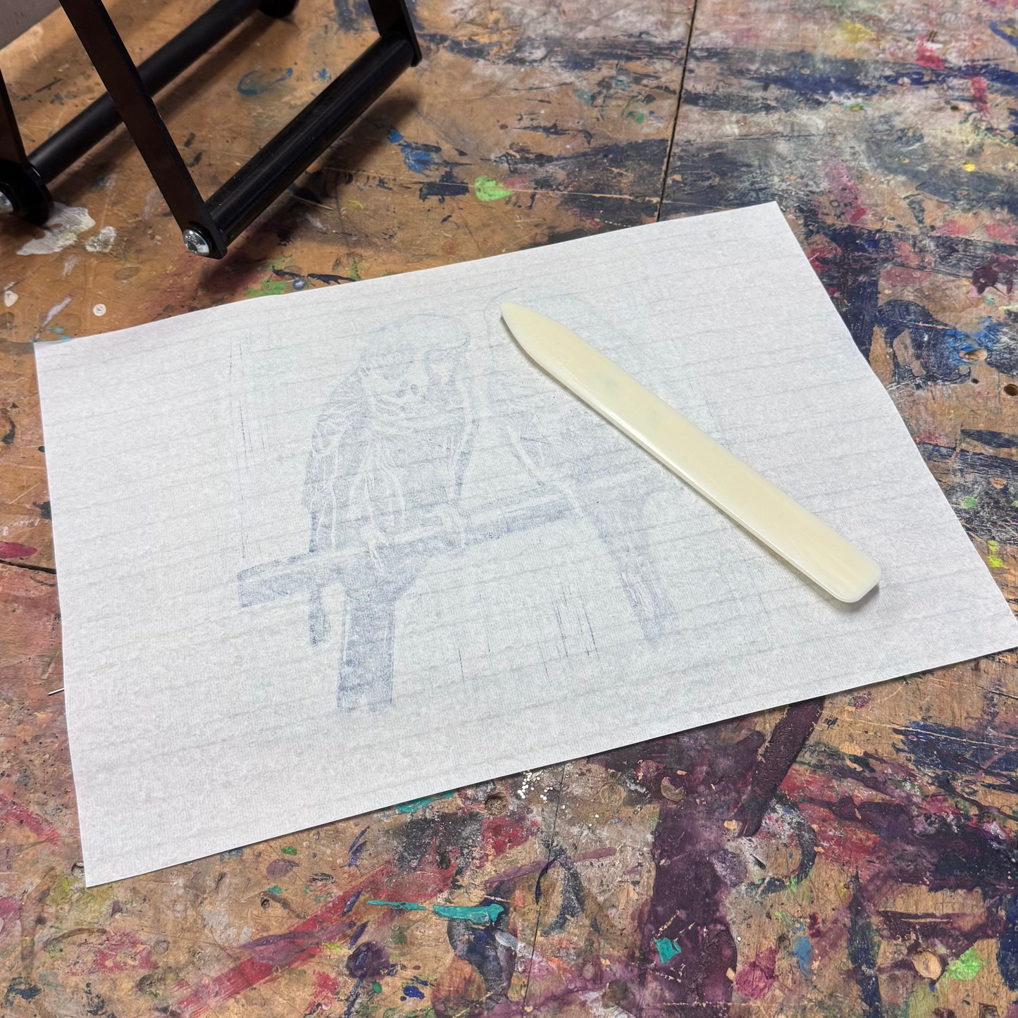 Artistic workspace with a piece of paper, knife, and cross-shaped object on a textured surface.